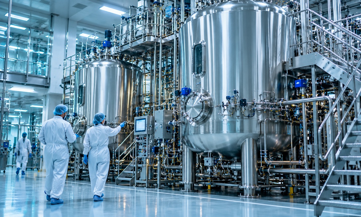 Operators beside large stainless-steel production bioreactors